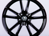 A black alloy car wheel is displayed with a five-spoke design, featuring the Volkswagen logo in the center, set against a plain white background.
