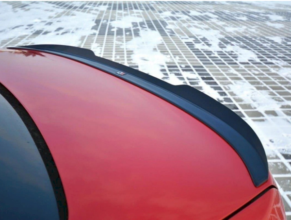A red car's rear spoiler sits prominently against a snowy, grid-patterned ground. A small emblem or badge is affixed to the spoiler's center.