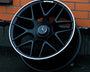 A black alloy wheel with a Mercedes emblem and "AMG" text is propped against an orange brick wall. The ground appears to be a dark, textured surface.