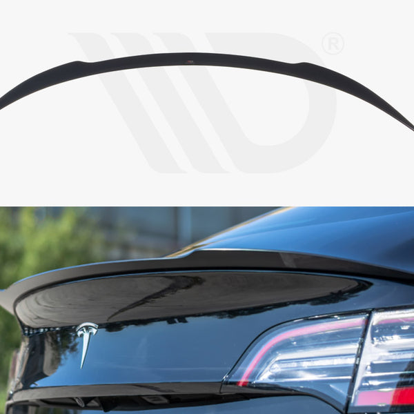 A black car spoiler is attached to the rear of a blue vehicle with a visible trunk emblem. The background is blurred, featuring greenery and a building.