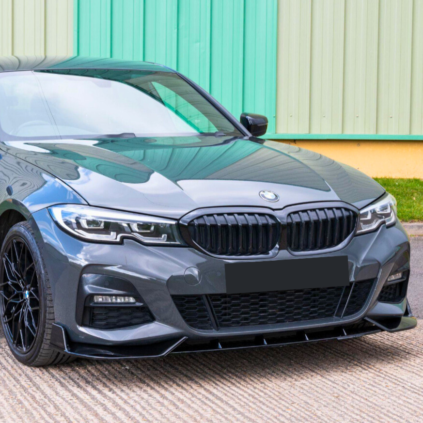 A gray BMW car is parked in front of a green and yellow corrugated building, showcasing its sleek front grille and headlights. The ground is paved with textured concrete.