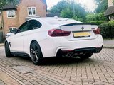 A white BMW 435d is parked on a brick driveway in a residential area, featuring distinctive dual exhausts and surrounded by houses and greenery.