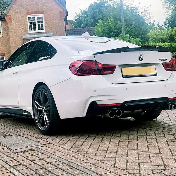 A white BMW 435d is parked on a brick driveway in a residential area, featuring distinctive dual exhausts and surrounded by houses and greenery.