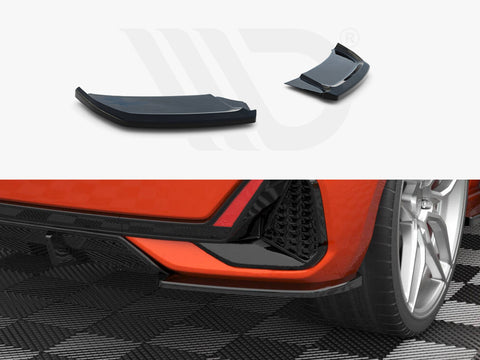 Two aerodynamic car accessories rest on a white surface, above a rear view of an orange car parked on a checkered floor, highlighting the vehicle's sleek design and wheels.