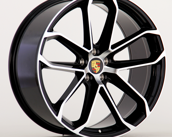A black and silver alloy wheel features the Porsche emblem at the center, with a modern, multi-spoke design. The wheel is set against a plain, light background.