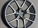 A silver alloy wheel with five double spokes, featuring a central Mercedes emblem, rests against a plain background. The rim displays the 