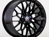 A black alloy wheel showcases a geometric, multi-spoke design, prominently featuring a BMW logo at its center against a plain, light gray background.
