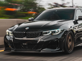A black car with sleek design speeds along a highway, surrounded by blurred greenery and streetlights, highlighting motion. The BMW logo is visible on the front grille.