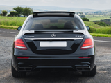 A black Mercedes-Benz E63S is parked on a paved road, with green fields and a cloudy sky in the background. Visible text: 