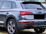 Audi SUV parked, rear view showcases stylish taillights, dual exhaust, and logo. The vehicle is parked on concrete near a building with large windows and curtains.