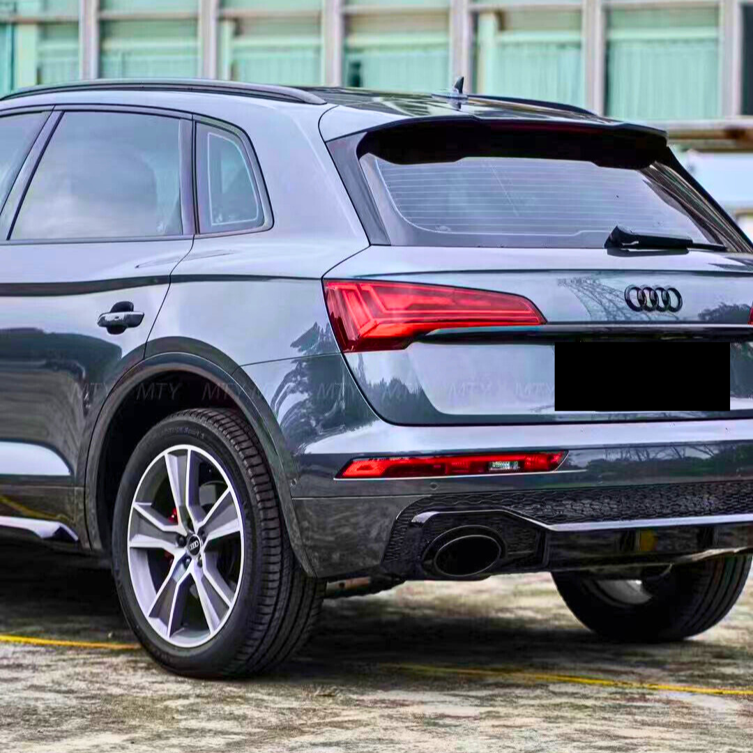 Audi SUV parked, rear view showcases stylish taillights, dual exhaust, and logo. The vehicle is parked on concrete near a building with large windows and curtains.