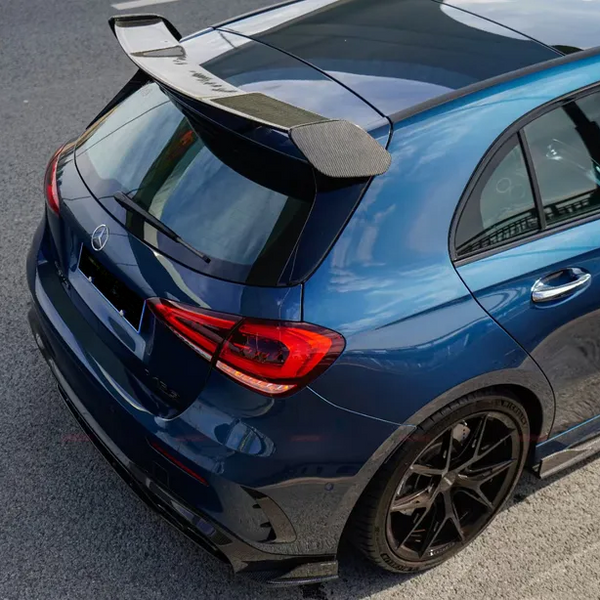 A blue car with a prominent rear spoiler is parked on a paved surface. The car features red taillights, a visible logo, and five-spoke black wheels.