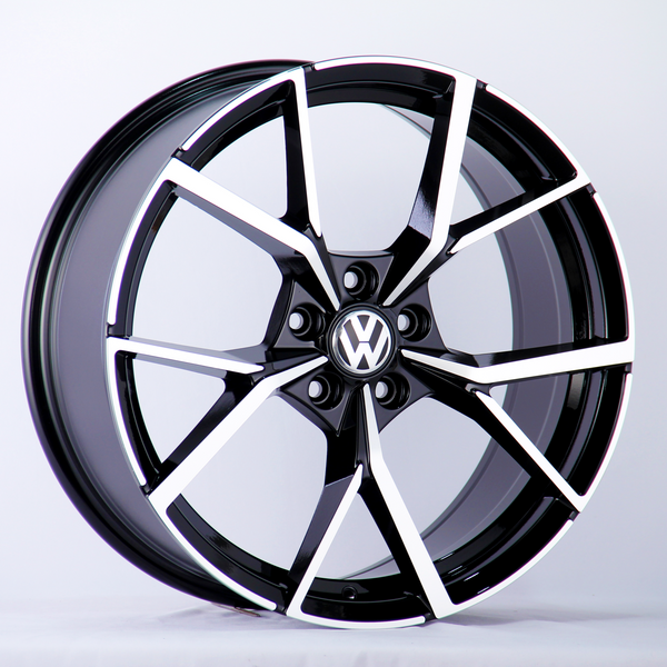 A black and silver alloy wheel with a Volkswagen logo in the center is positioned upright against a plain white background, highlighting its intricate spoke design.