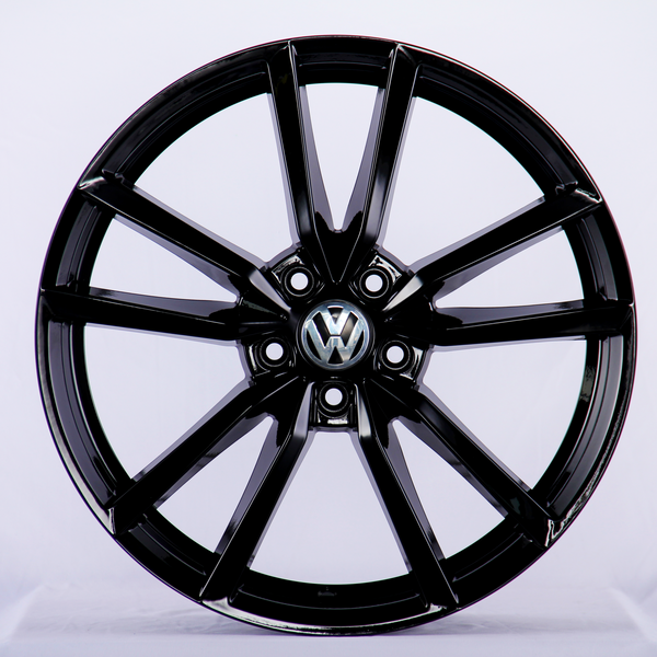 A shiny black car wheel features multiple spokes radiating from a central hub with the Volkswagen logo. It's displayed against a plain white background.