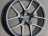 A Mercedes-Benz alloy wheel stands upright, featuring a five-spoke design with a polished finish. The AMG logo is inscribed at the top. It's set against a neutral background.