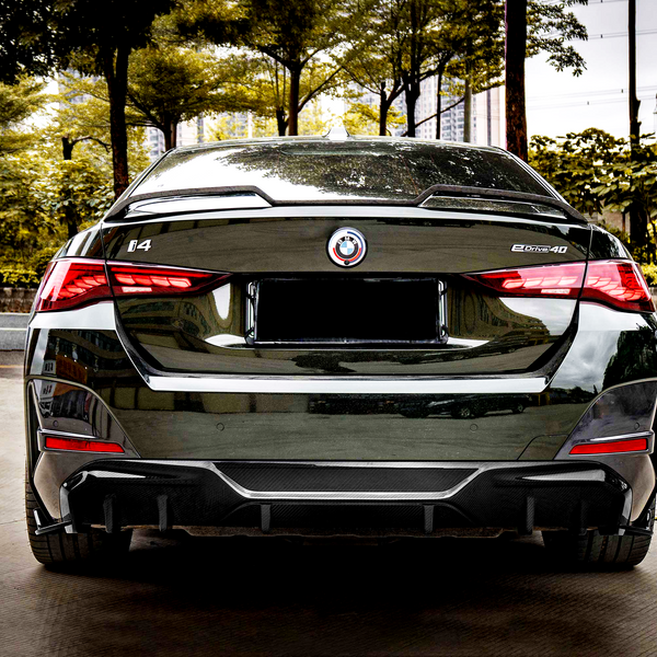 A sleek black car is parked, displaying a rear view with red taillights illuminated. The environment features green trees and a city street. Visible text includes: "i4" and "eDrive40."