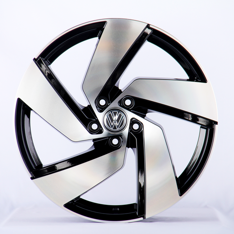 A metallic car wheel rim with a five-spoke design features a central logo containing a "VW" emblem, displayed against a plain white background.