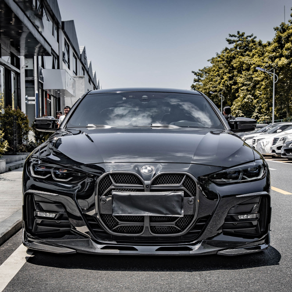 A black BMW car is parked on a street, facing forward. It features a prominent front grille and sits beside a row of buildings with trees lining the street.
