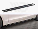 Two long, narrow black side skirt extensions displayed above the side profile of a white car. The car is parked on a textured floor, enhancing its sporty appearance.