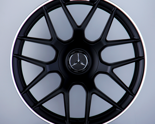 A black alloy wheel with a Mercedes emblem and "AMG" text, mounted vertically on a display stand against a plain gray background.