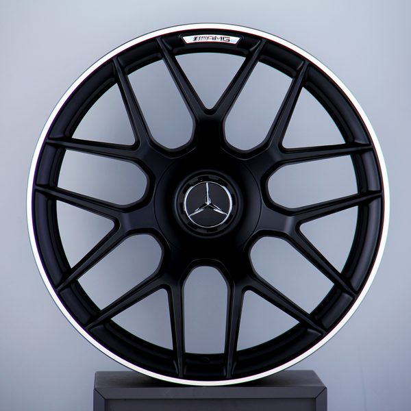 A black alloy wheel with a Mercedes emblem and "AMG" text, mounted vertically on a display stand against a plain gray background.
