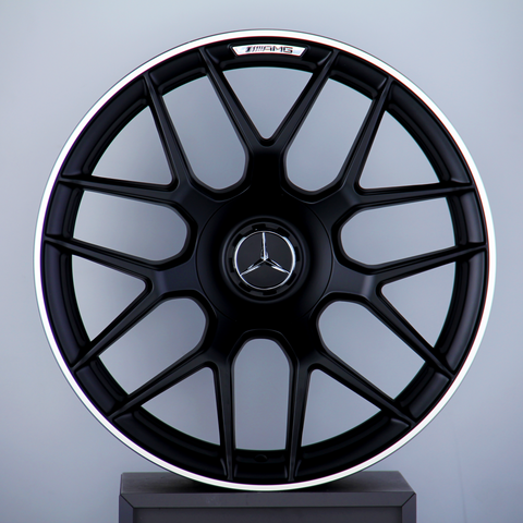 A black alloy wheel with a Mercedes emblem and "AMG" text, mounted vertically on a display stand against a plain gray background.