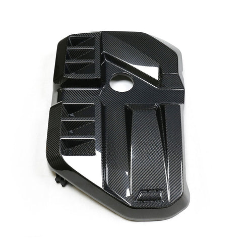 A carbon fiber engine cover with geometric patterns and a circular cutout, placed on a plain white background.