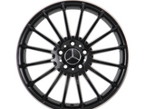 A black alloy wheel with multiple spokes featuring a central emblem resembling interlocking triangles; it is isolated on a white background, showcasing its symmetrical design.
