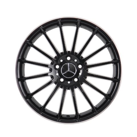 A black alloy wheel with multiple spokes featuring a central emblem resembling interlocking triangles; it is isolated on a white background, showcasing its symmetrical design.