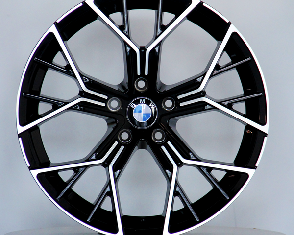 A black and silver alloy wheel with a BMW logo rests vertically on a round white platform against a plain grey background.