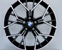 A black and silver alloy wheel with a BMW logo rests vertically on a round white platform against a plain grey background.