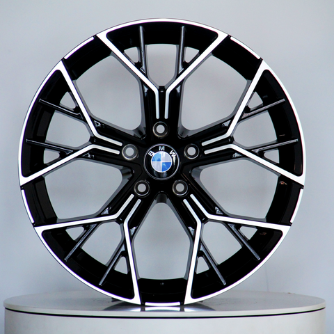 A black and silver alloy wheel with a BMW logo rests vertically on a round white platform against a plain grey background.