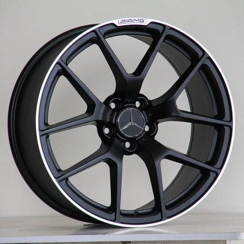 A black alloy wheel with a silver Mercedes logo, features the text "AMG" above the rim. It rests on a light surface against a plain background.