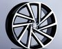 A polished, black-and-silver car wheel rim is displayed upright, featuring a VW logo at its center, against a softly lit, plain gray background.