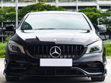 A black Mercedes-Benz car is parked outdoors, facing forward. The background consists of greenery and a multi-story building.