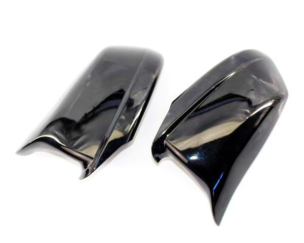 Two glossy black plastic car mirror covers, positioned side by side, reflecting light on a plain white background.
