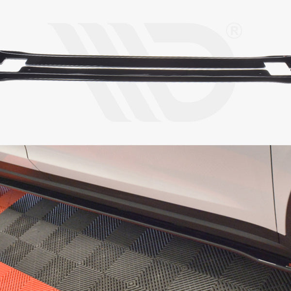 A black car side skirt lies on a textured floor, with a white vehicle parked nearby, partially showing the skirt attached. The background has a mix of red and gray patterns.