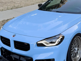 A sleek, blue sports car is parked on a road next to a grassy area, featuring a glossy black roof and distinctive front bumper with an 