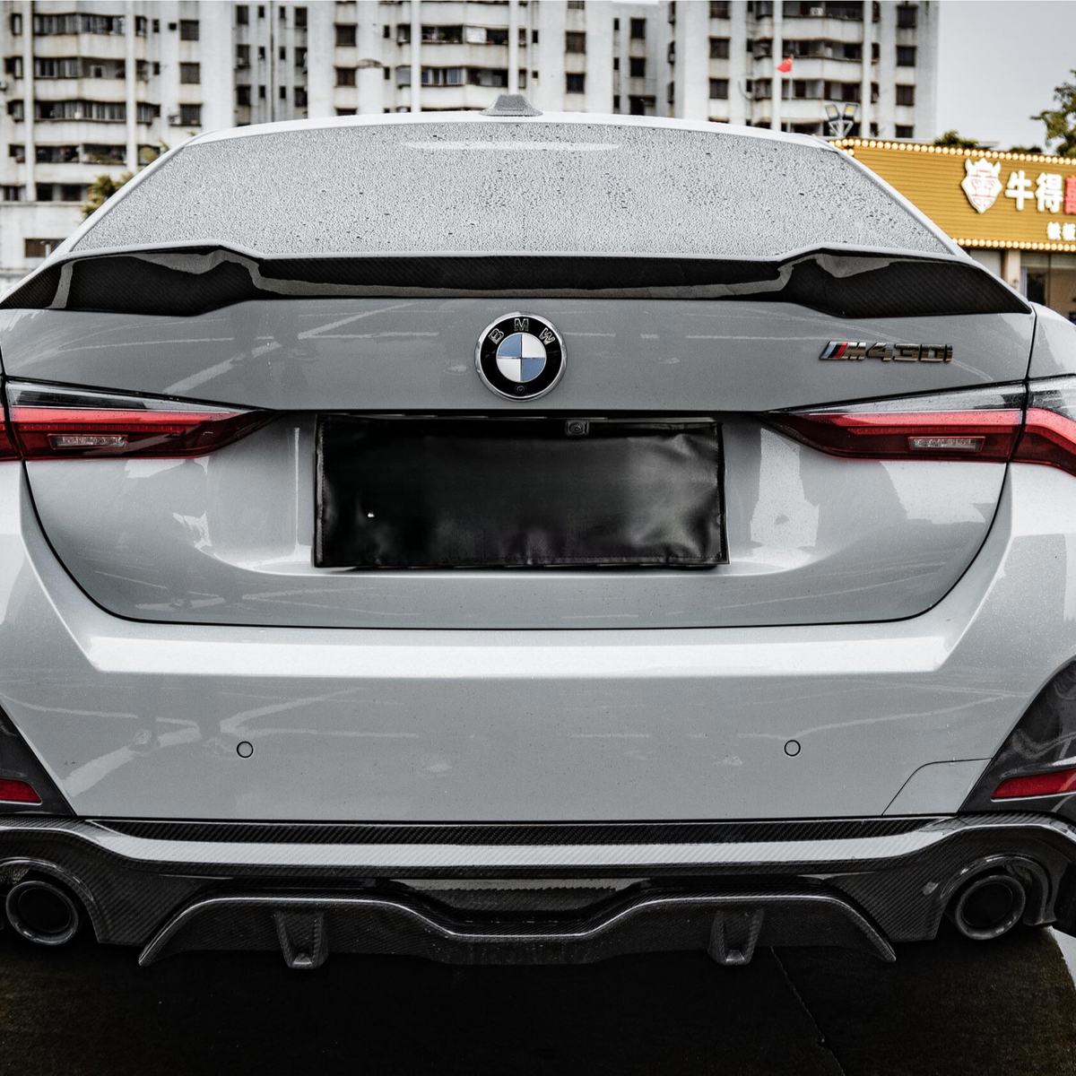 A gray BMW car is parked in a wet urban area near a building with Chinese signage, featuring distinctive taillights and a sporty rear bumper.