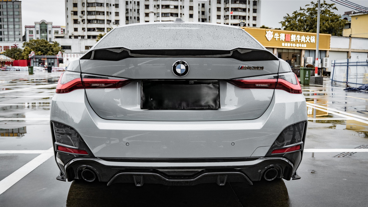 A gray BMW car is parked in a wet urban area near a building with Chinese signage, featuring distinctive taillights and a sporty rear bumper.