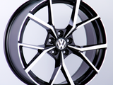 A black and silver alloy wheel is displayed upright. The wheel features the Volkswagen logo in the center, set against a plain white background.