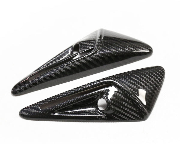 Two carbon fiber objects feature a sleek, aerodynamic design with pointed ends and small circular cutouts, set against a plain white background.
