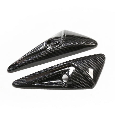 Two carbon fiber objects feature a sleek, aerodynamic design with pointed ends and small circular cutouts, set against a plain white background.