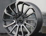 A polished silver and black alloy wheel rests upright on concrete. "Range Rover" is inscribed at its center. The background is blurred, suggesting an urban setting.