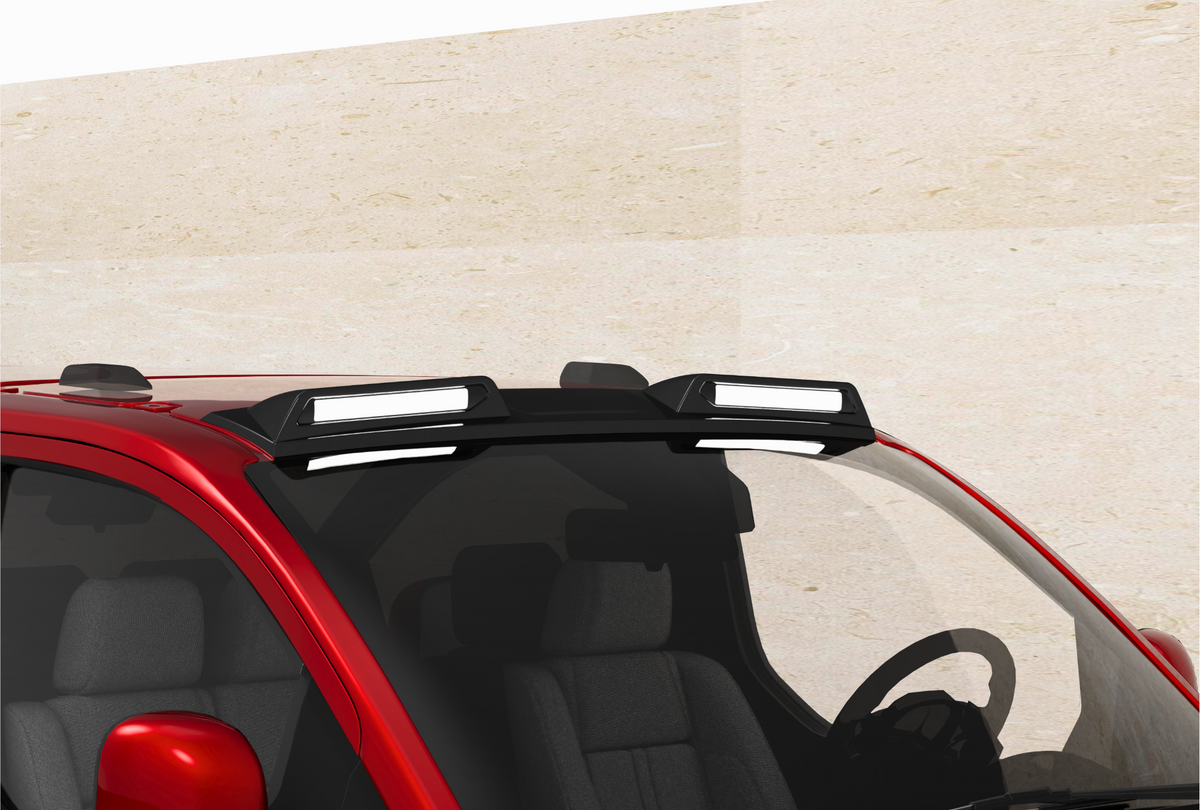 A red car with a roof rack mounted, holding two rectangular lights. The vehicle is parked against a plain, beige wall, seen from a slightly elevated front angle.