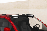 A red car with a roof rack mounted, holding two rectangular lights. The vehicle is parked against a plain, beige wall, seen from a slightly elevated front angle.