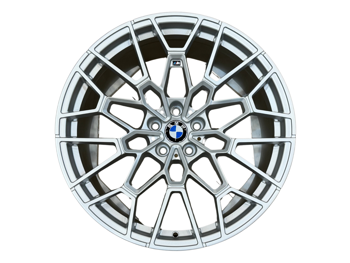 A silver alloy wheel with intricate spoke design, featuring a central blue and white logo, set against a plain white background.