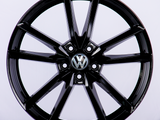 A shiny black, multi-spoke alloy wheel featuring a central Volkswagen logo, displayed against a plain white background.