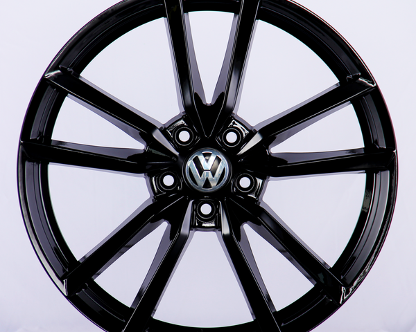 A shiny black, multi-spoke alloy wheel featuring a central Volkswagen logo, displayed against a plain white background.