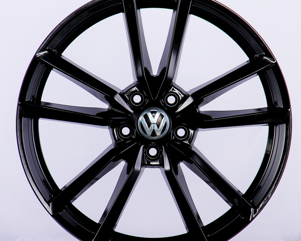 A glossy black alloy wheel with a multi-spoke design, featuring a Volkswagen emblem at the center, set against a plain white background.